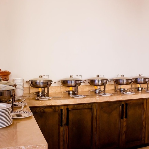 Un mostrador de buffet con varios rechauds de acero inoxidable y montones de platos y cuencos está preparado para servir comida.