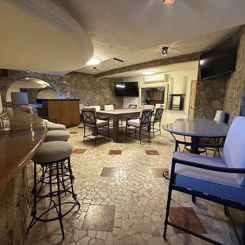 Una amplia sala de entretenimiento presenta paredes de piedra, un suelo de mosaico, una barra de bar y varias áreas de asiento y mesas.