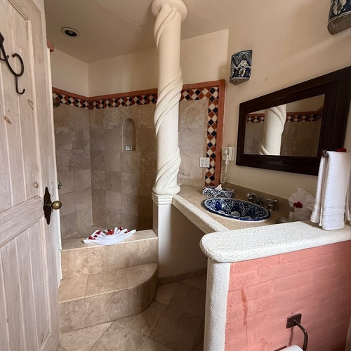 Un baño de estilo rústico mexicano presenta una ducha con escalones, un lavabo de cerámica azul pintado a mano y una columna salomónica central.