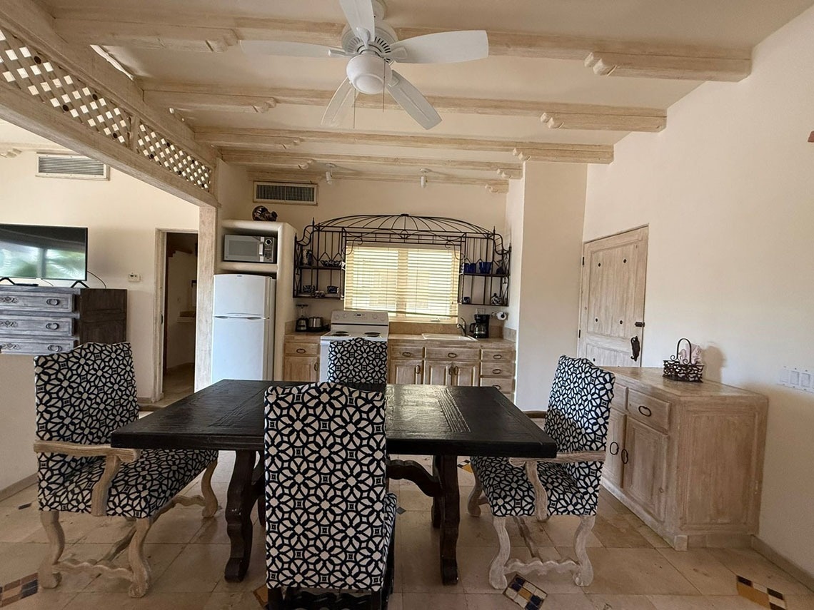 Un comedor rústico con un área de cocina adjunta, que presenta vigas de madera expuestas en el techo y mobiliario de madera clara.