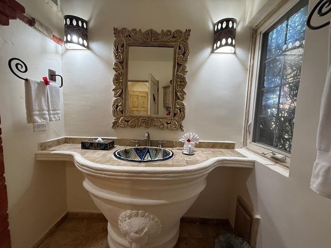 Un cuarto de baño de estilo rústico presenta un lavabo artesanal, un espejo ornamentado y apliques de pared.