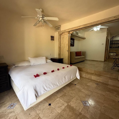 Una acogedora habitación con una cama grande decorada con pétalos rojos, un ventilador de techo y suelo de baldosas, que se conecta a una sala de estar a un nivel inferior.