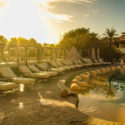 Una piscina de resort con tumbonas y cabañas bajo un sol dorado y brillante.