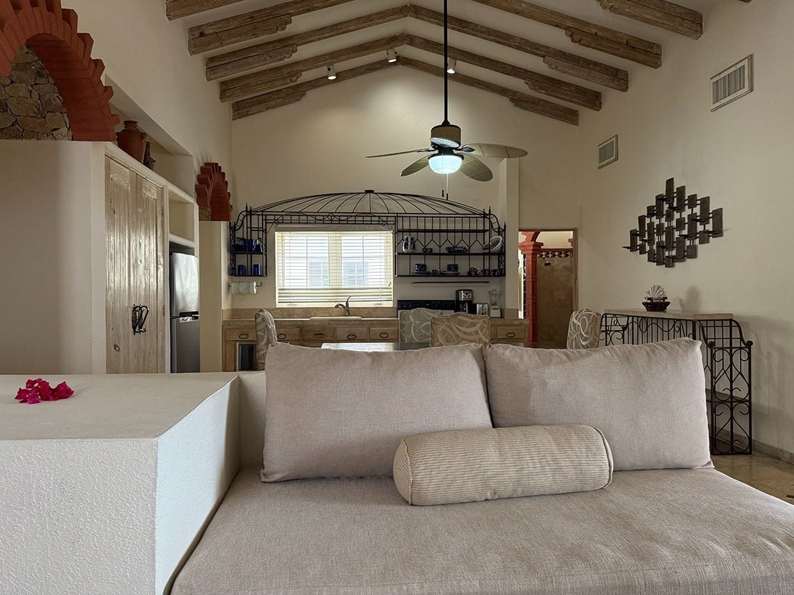 Un amplio salón-comedor con techos abovedados y vigas de madera expuestas, decorado con un estilo rústico y toques mexicanos, se extiende hacia una cocina abierta al fondo.