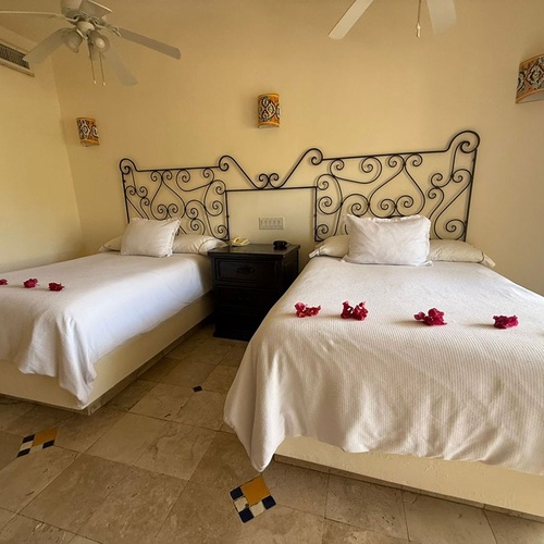 Una habitación con dos camas individuales, cabeceros de hierro forjado y decoradas con pétalos de flores rojas.