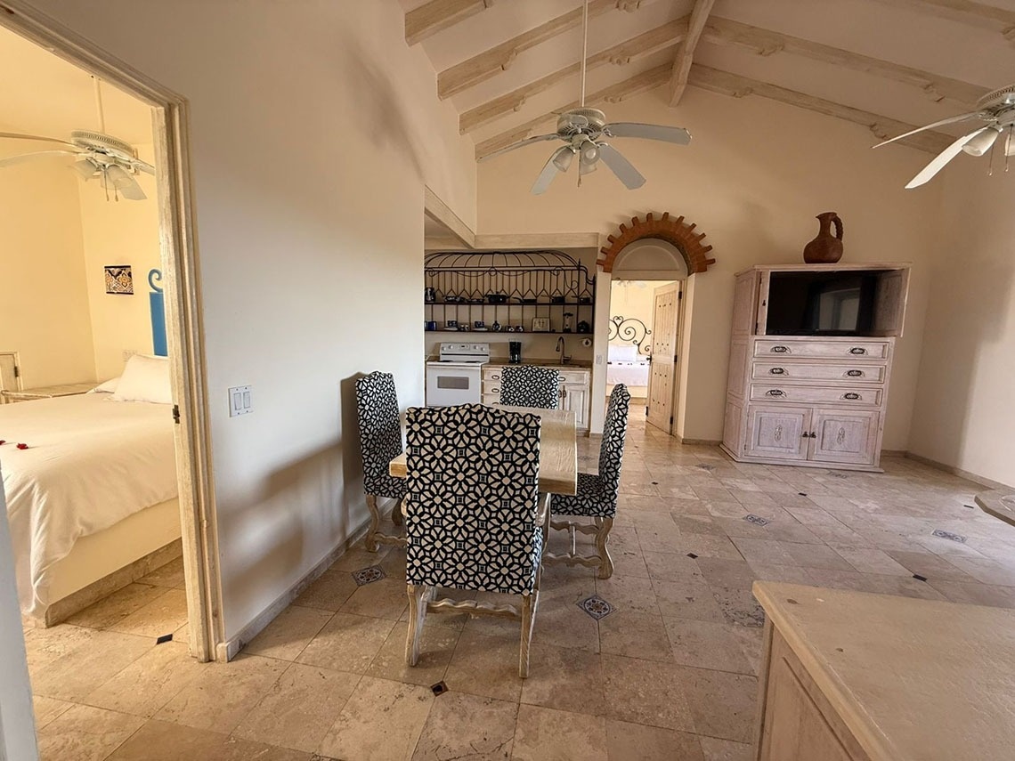 Un espacio interior que presenta una sala de estar, comedor y cocina compacta, con acceso a un dormitorio y decorado con techos abovedados y suelos de azulejos.