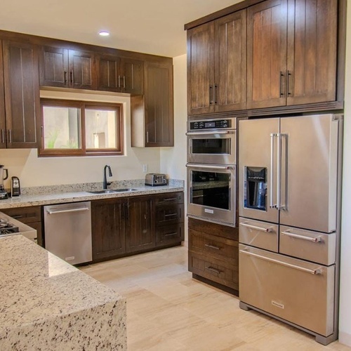Cocina moderna con gabinetes de madera oscura, encimeras de granito claro y electrodomésticos de acero inoxidable.