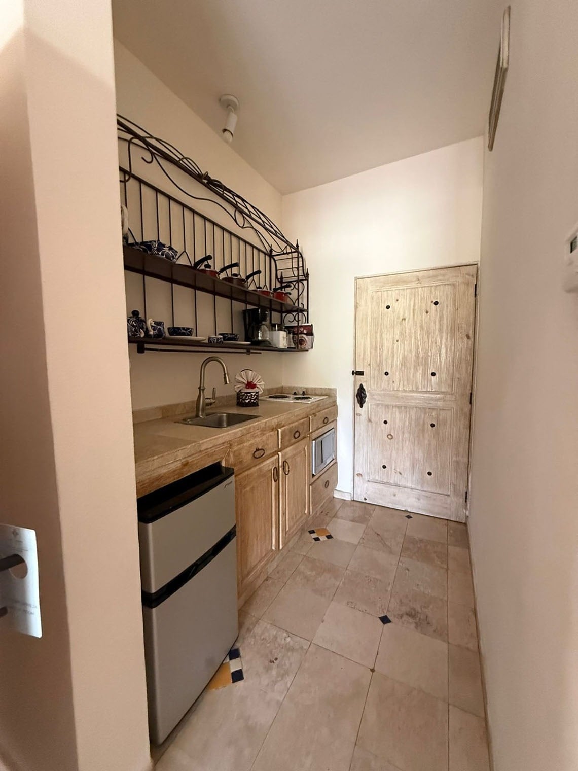 Una pequeña cocina de estilo rústico equipada con encimera, fregadero, nevera, microondas y estantes de hierro forjado.