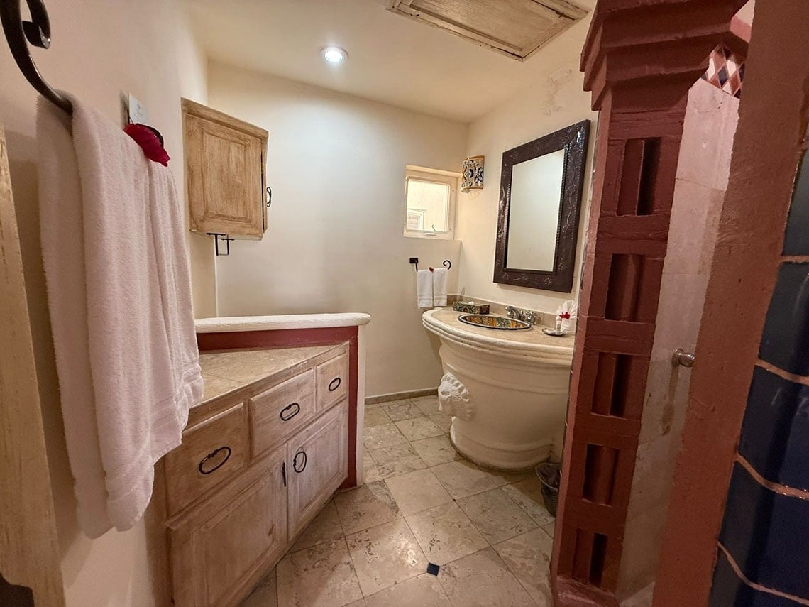 Un cuarto de baño de estilo rústico y tradicional con un lavabo de pedestal esculpido, un tocador de madera clara y una entrada a la ducha.