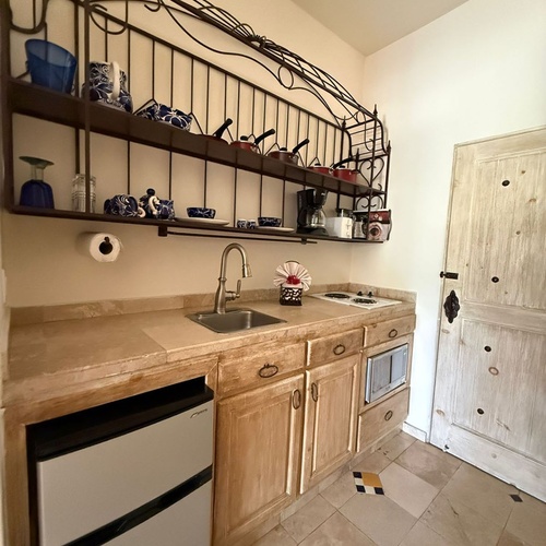 Cocina compacta de estilo rústico con encimeras de piedra, estantería de hierro forjado y una puerta de madera envejecida.