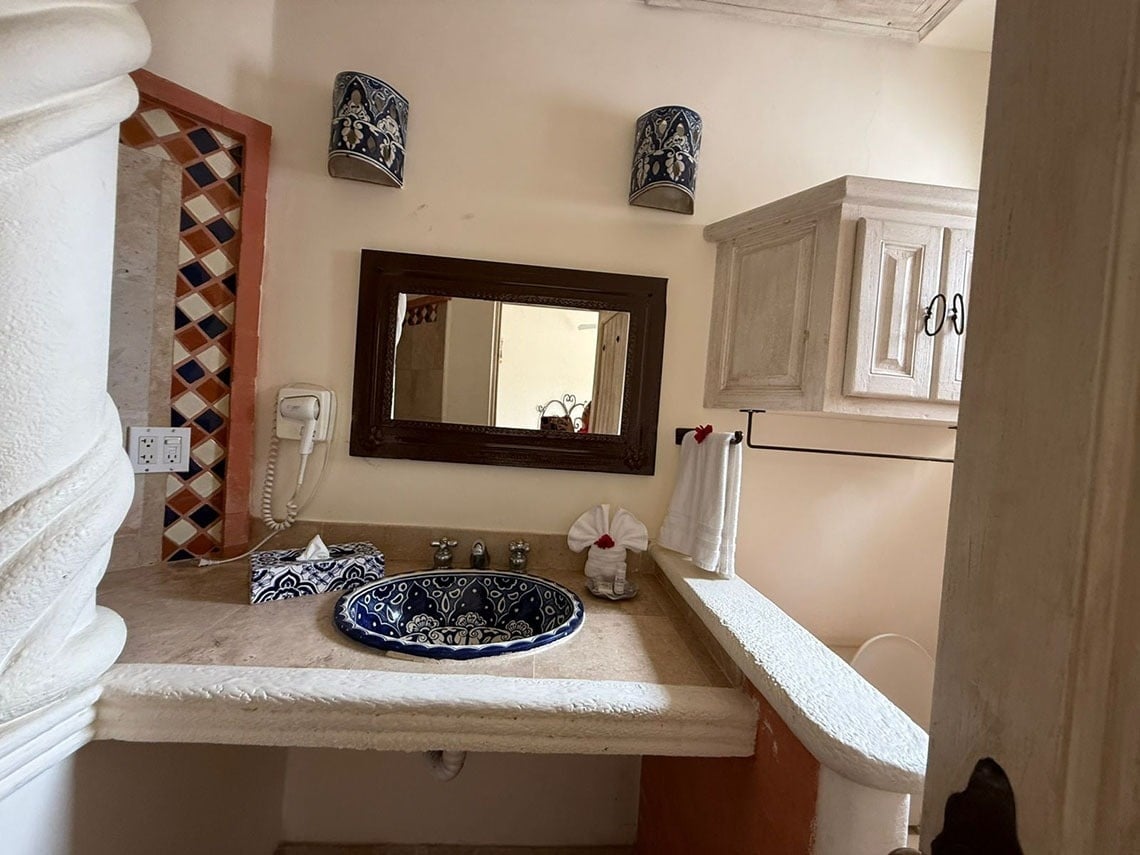 Un tocador de baño de estilo rústico con un lavabo de cerámica azul y blanca decorada, un espejo con marco de madera y apliques de pared ornamentados.