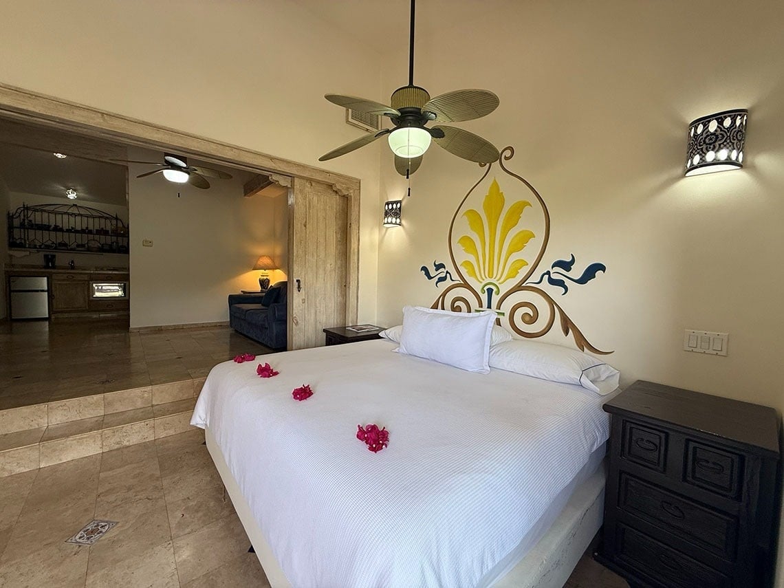 Una habitación con una cama grande y un mural decorativo, que da a un espacio con cocineta y sala de estar a un nivel inferior.