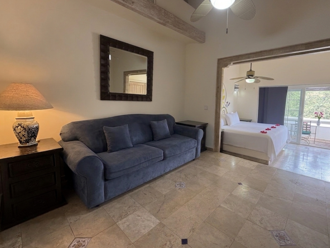 A spacious room is divided into a bedroom with a decorative headboard and a living area with a blue sofa, both featuring ceiling fans and tiled floors.