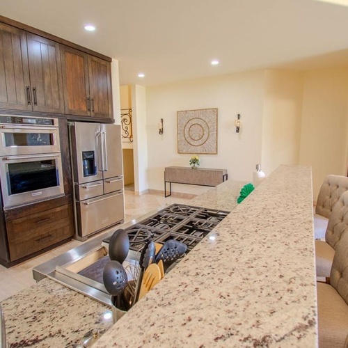 Una cocina moderna con gabinetes de madera oscura, electrodomésticos de acero inoxidable y una isla grande con estufa y taburetes.