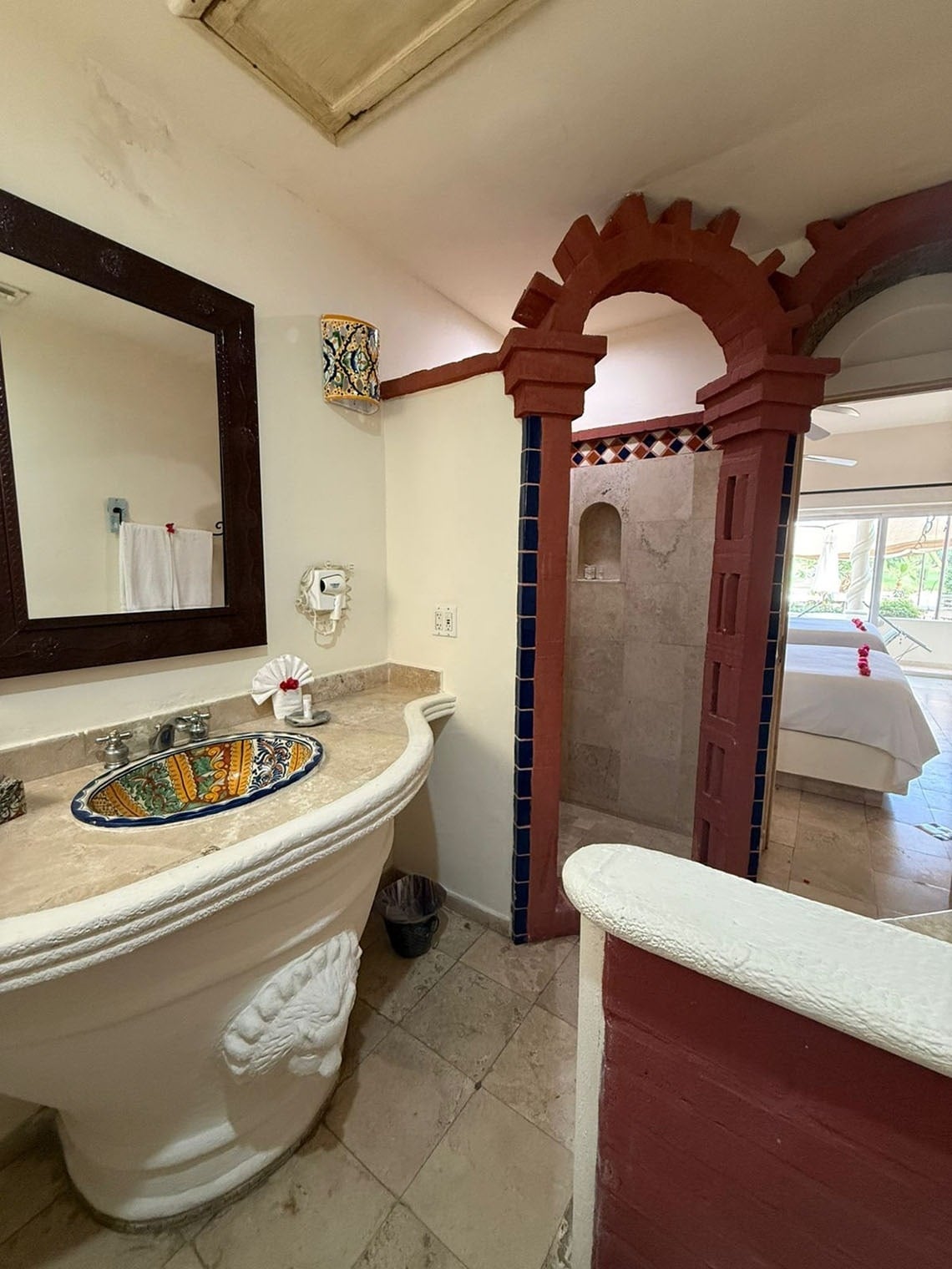 La imagen muestra un baño de estilo mexicano con un lavabo decorativo, una ducha abovedada y una conexión abierta a un dormitorio.