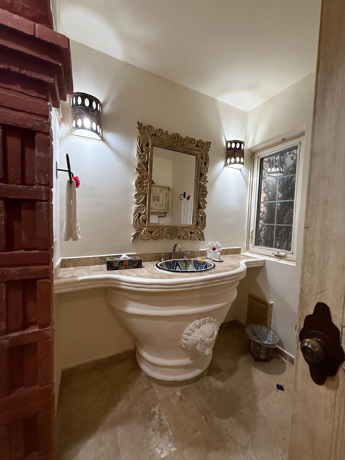 Un baño de estilo rústico y tradicional con un lavabo de pedestal esculpido, un espejo ornamentado y apliques de pared.