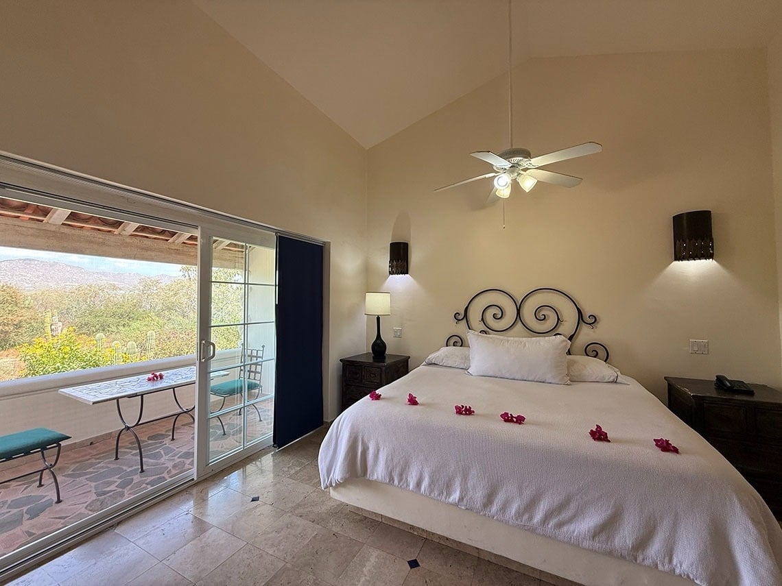 Un dormitorio acogedor con una cama grande y una puerta corredera de cristal que da a un balcón con vistas a un paisaje verde y montañoso.