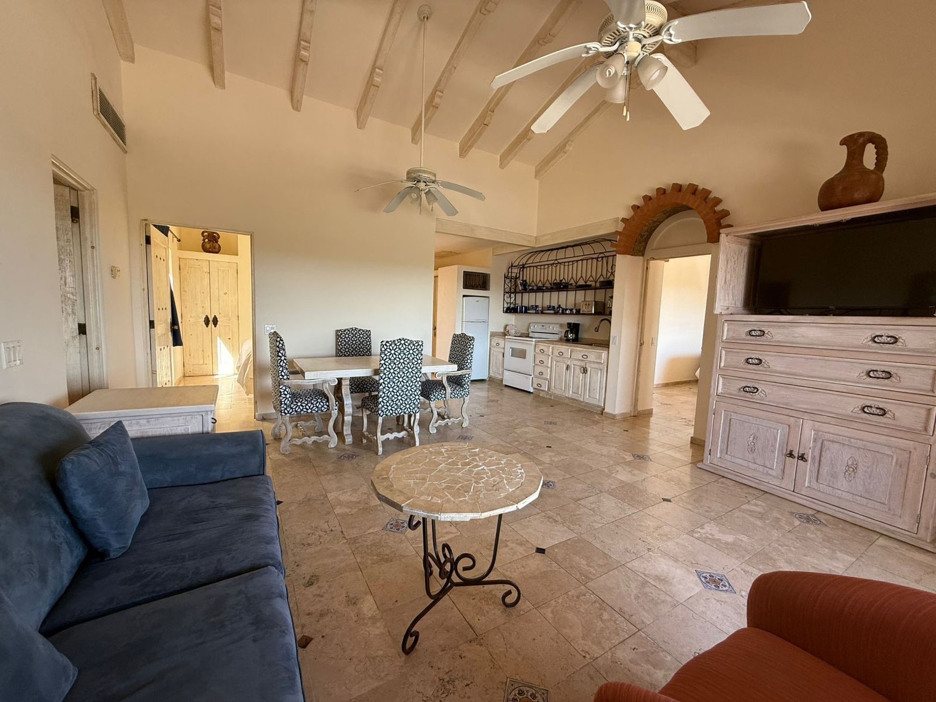 Un amplio espacio interior de concepto abierto que combina sala de estar, comedor y cocina, decorado con muebles rústicos, techos con vigas expuestas y suelos de baldosas.