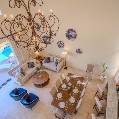 Una vista aérea muestra un espacioso interior de planta abierta con sala de estar, comedor y cocina, destacando un gran candelabro y una piscina exterior.