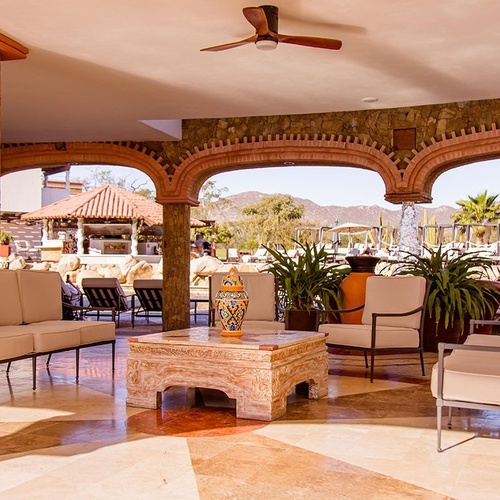 Una amplia terraza cubierta con arcos de piedra y ladrillo, mobiliario de exterior y vistas a un paisaje montañoso y una piscina.