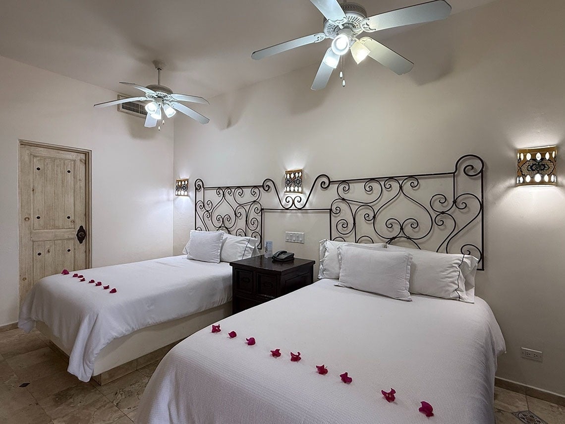 Una habitación de hotel acogedora con dos camas individuales, cabeceras de hierro forjado, apliques de pared ornamentados y ventiladores de techo.