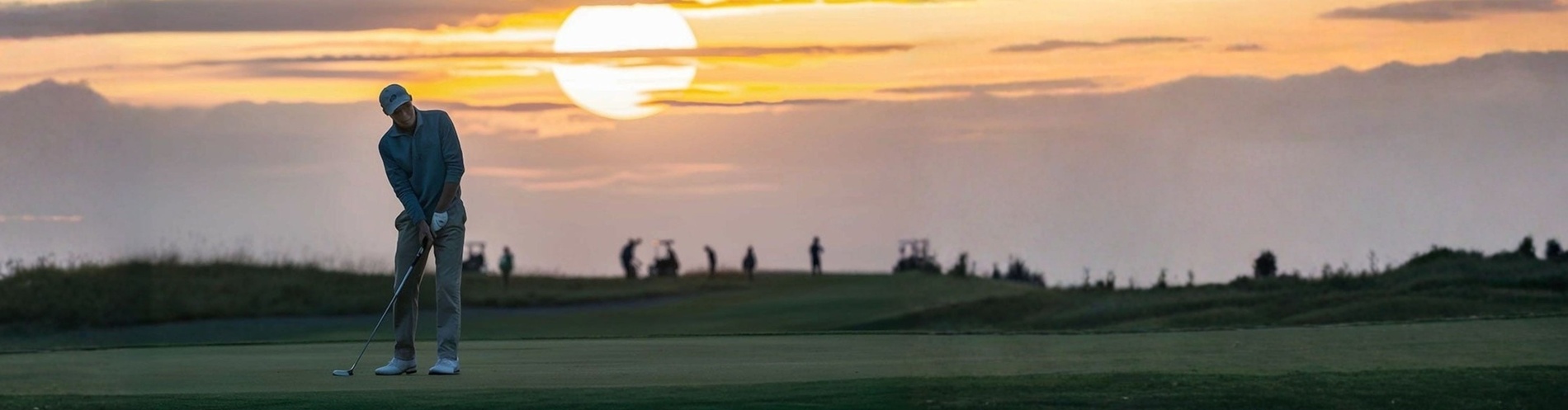 A golfer putts on a green at sunset, with a large, bright sun illuminating the sky and other figures in the blurred background.