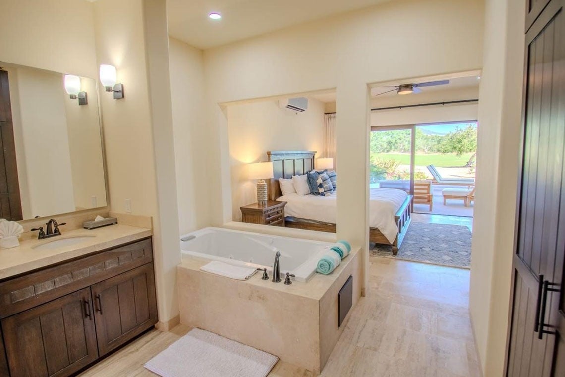 Una suite de concepto abierto con un área de baño que incluye bañera y lavabo, conectada a un dormitorio con una cama y vista a un patio exterior.