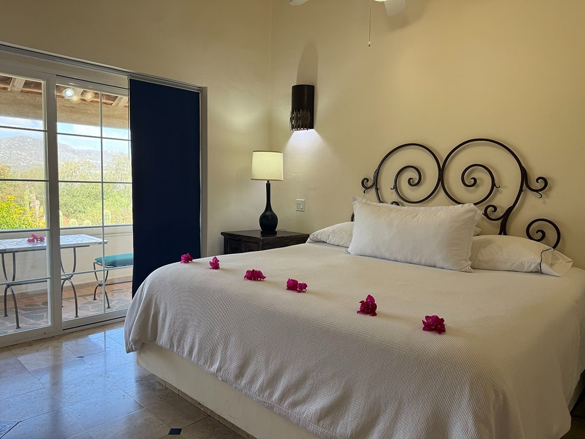 Dormitorio con cama decorada con flores y un balcón con vistas a la montaña.