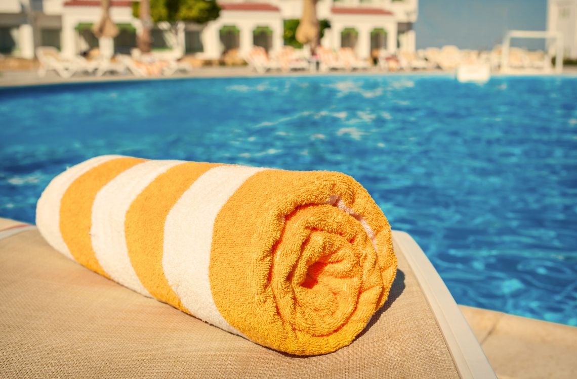 Una terraza al aire libre decorada con guirnaldas de luces ilumina cómodos asientos y mesas de comedor al atardecer, con un campo de golf y una piscina al fondo.