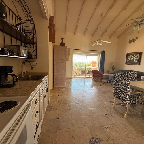 Una cocina y comedor con vista a una sala de estar, que se abre a un balcón con vista al exterior.