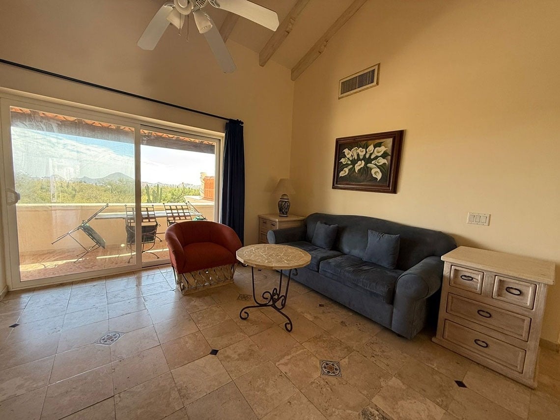 Una luminosa sala de estar con sofá, sillón y piso de baldosas, que se abre a un balcón con vistas a la naturaleza.