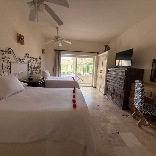 Una habitación de hotel con dos camas, cabeceros de hierro forjado, un televisor y un balcón, decorada con muebles de madera y azulejos.