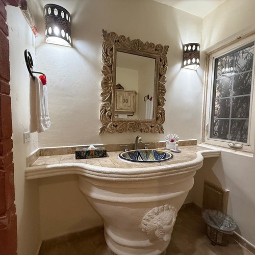 Un baño con un lavabo de pedestal esculpido, un espejo ornamentado y apliques de pared decorativos.