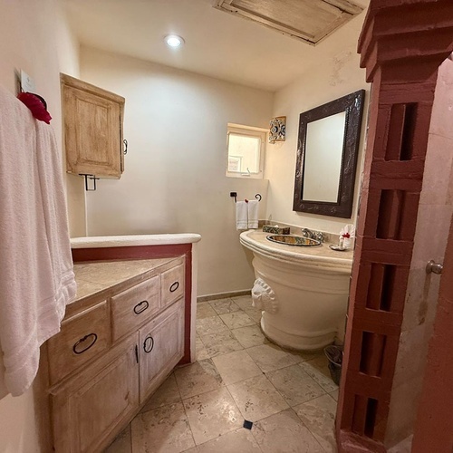 Un baño de estilo colonial mexicano con un singular lavabo de pedestal, un mueble de madera y una ducha con mampostería roja.