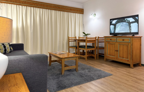 A stone bathroom counter with a sink, potted orchids, and a note sits below hanging white towels and a large mirror reflecting a toilet.