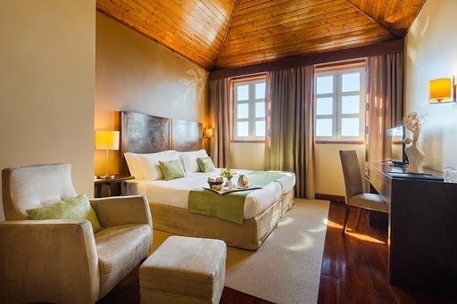 Um quarto de hotel bem iluminado com teto de madeira, cama, poltrona e secretária, exibindo uma decoração acolhedora.