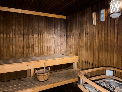 Uma sauna de madeira aconchegante com bancos, um balde com concha, um aquecedor e instrumentos de medição na parede.