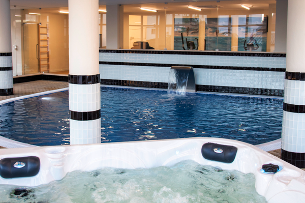 Indoor swimming pool and jacuzzi at hotel spa, with gym visible in background. Luna Corporativa