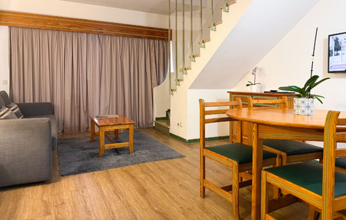 A brightly lit kitchen features a tiled backsplash with green and white stripes, a stainless steel sink, a toaster, a kettle, an induction cooktop, and built-in white appliances including a dishwasher and microwave.