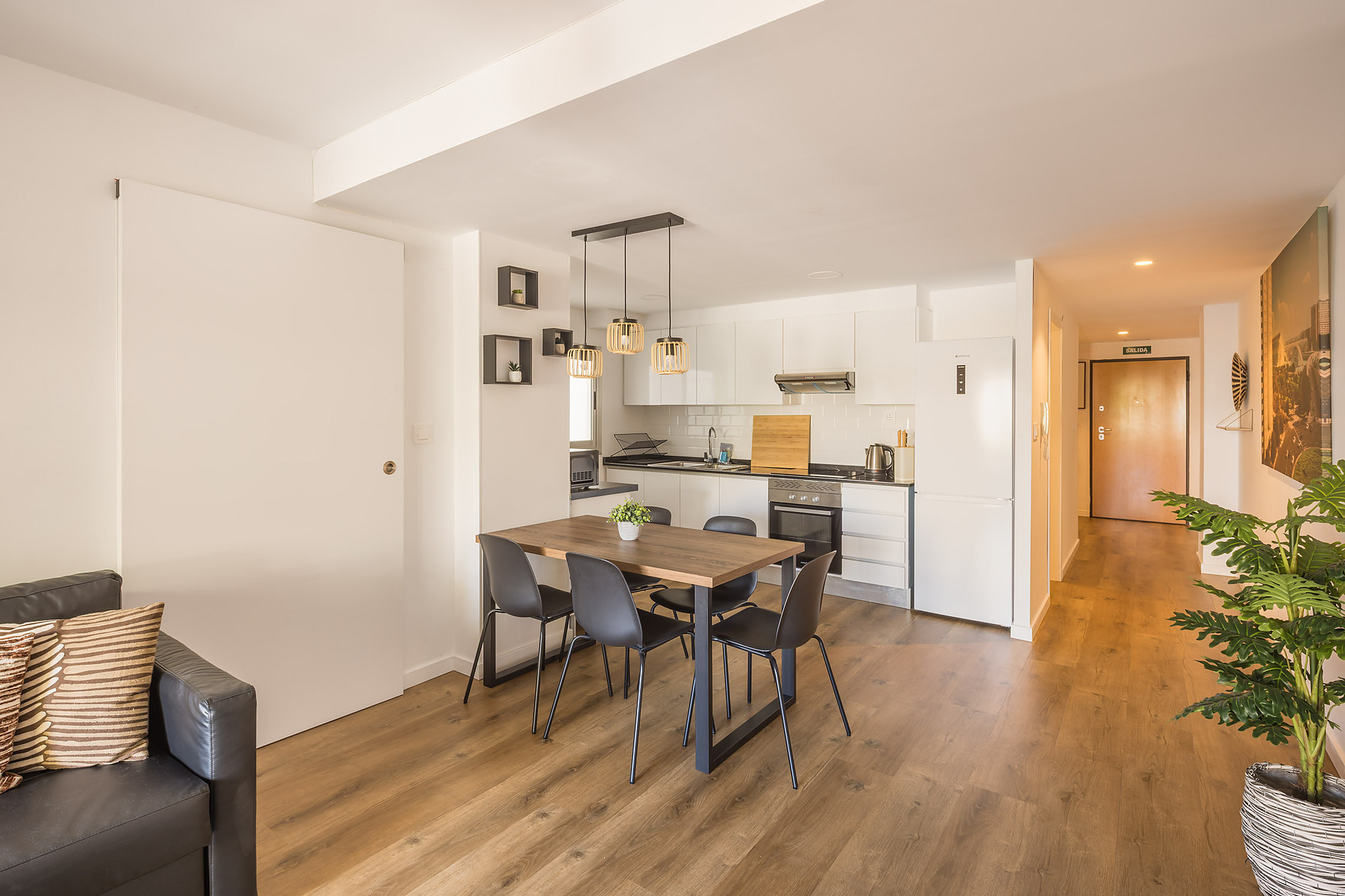 Modern open-plan dining and kitchen area in a hotel room Macflats: Ciudad de las ciencias with a wooden table, black chairs, and a sleek white kitchen.