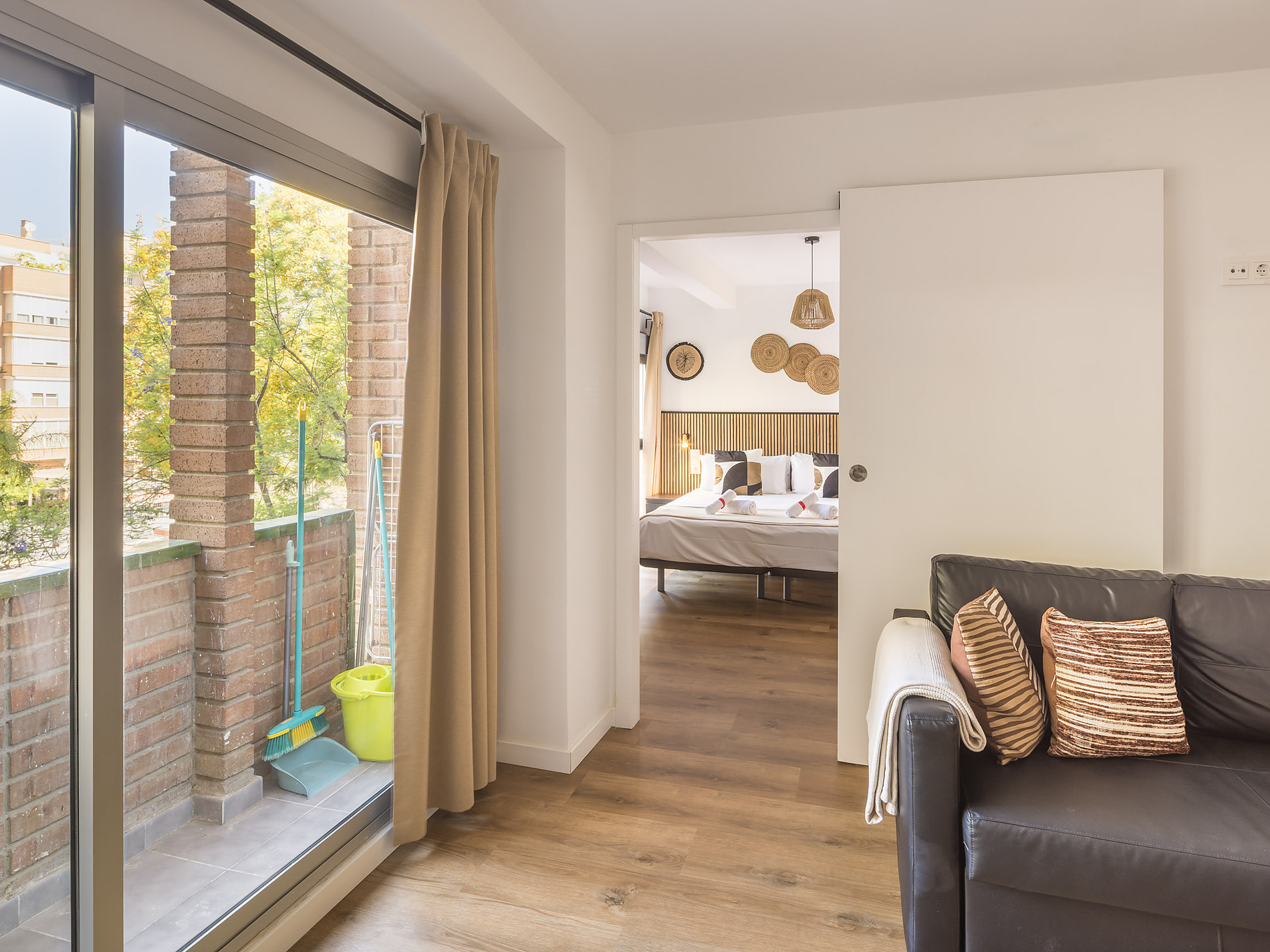 Macflats: Ciudad de las ciencias living area with view of a bedroom, balcony with cleaning supplies, and a leather sofa.