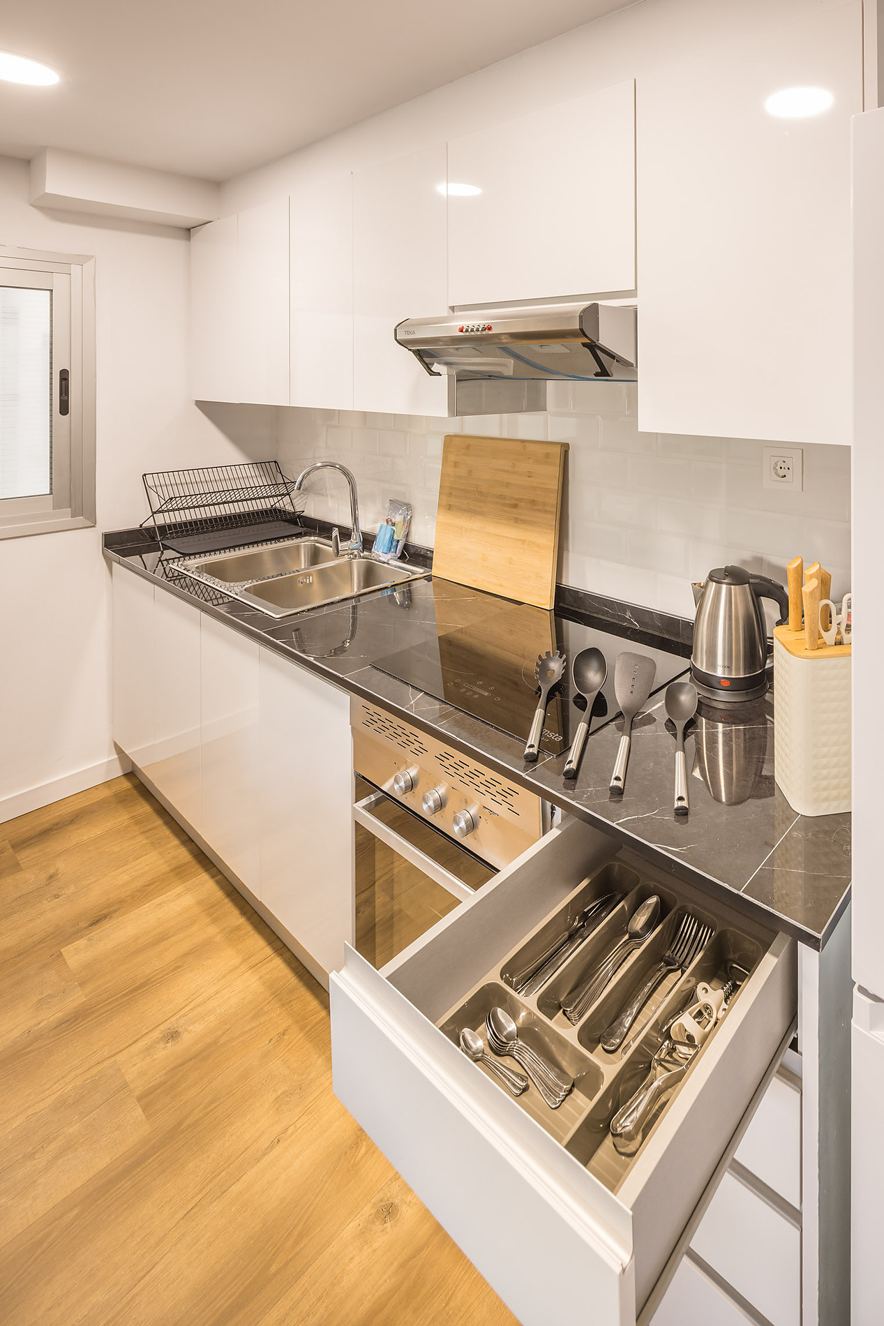 Modern kitchen with stainless steel appliances, sink, and an open cutlery drawer. Macflats: Ciudad de las ciencias