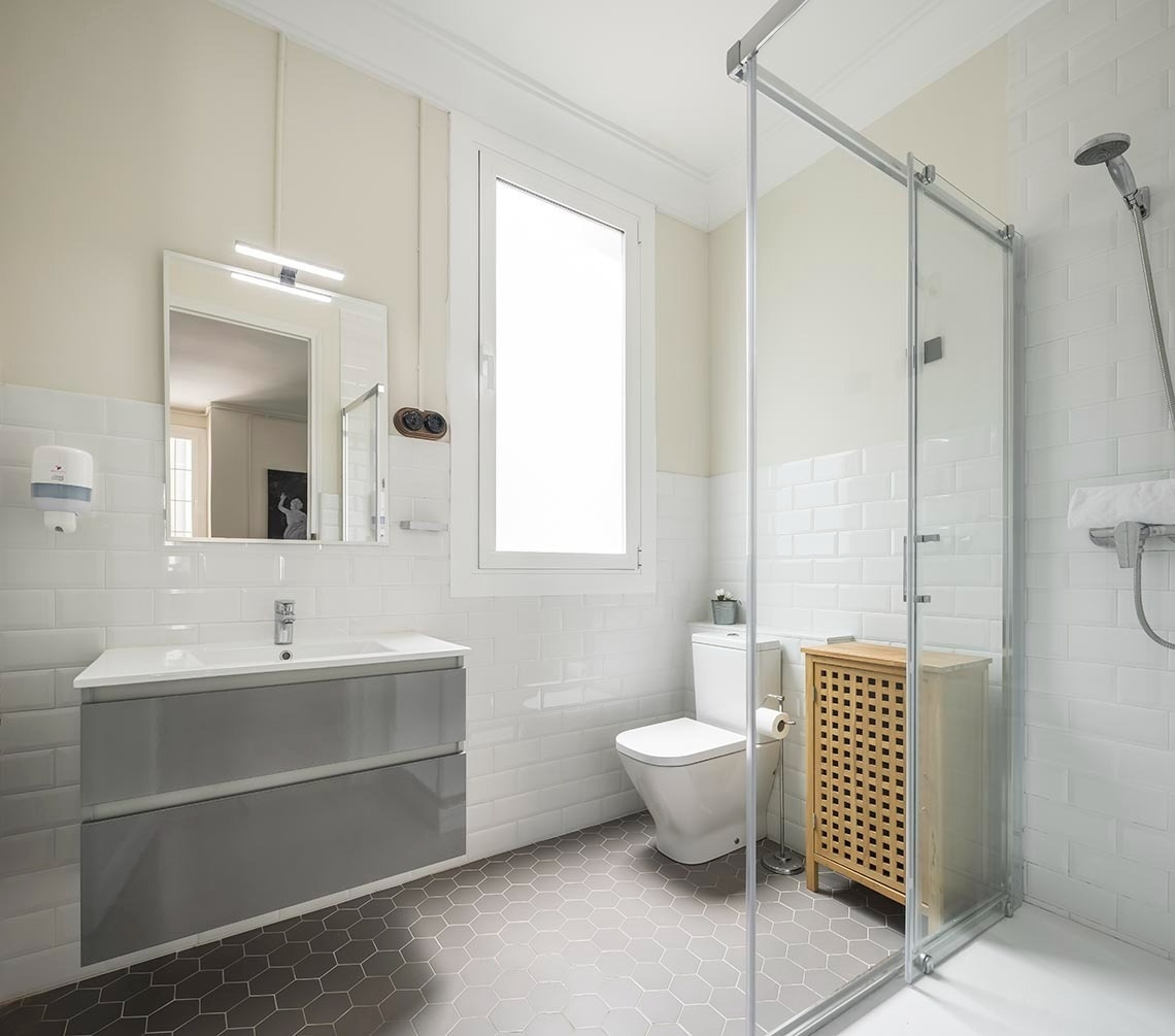 Baño moderno en Macflats Ayuntamiento | Macflats Valencia, con ducha cristal, lavabo gris y suelo hexagonal.