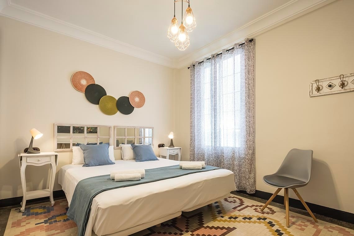 Dormitorio moderno Macflats Ayuntamiento Valencia: cama doble, mesas de noche, ventana y silla.