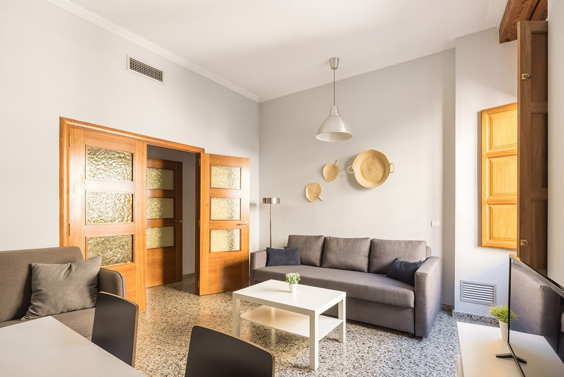 Salón de Macflats Apartamento Puerto | Sofá gris, mesa café, puertas de madera y decoración mural.