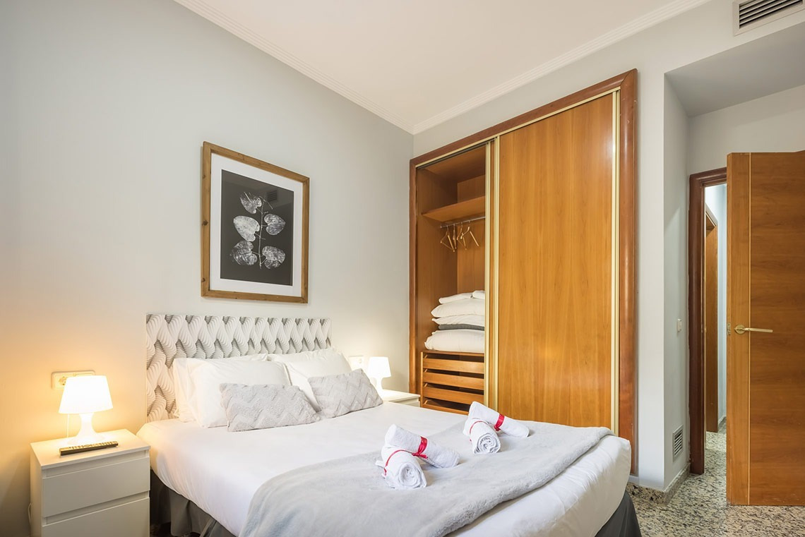 Habitación luminosa con cama cómoda, armario de madera y cuadro en Macflats Apartamento Puerto | Macflats Valencia | Web oficial.