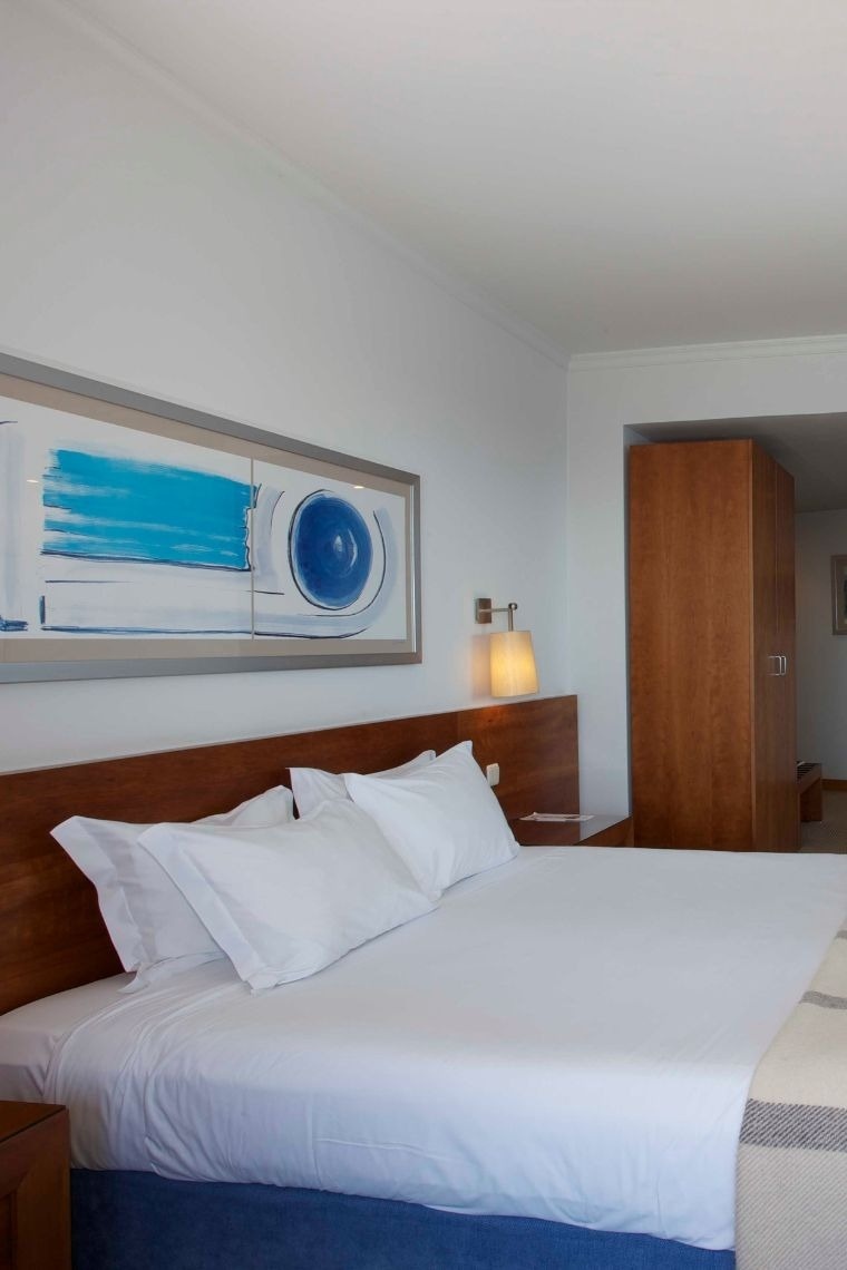 um quarto de hotel com uma cama king size e uma pintura sobre a cabeceira