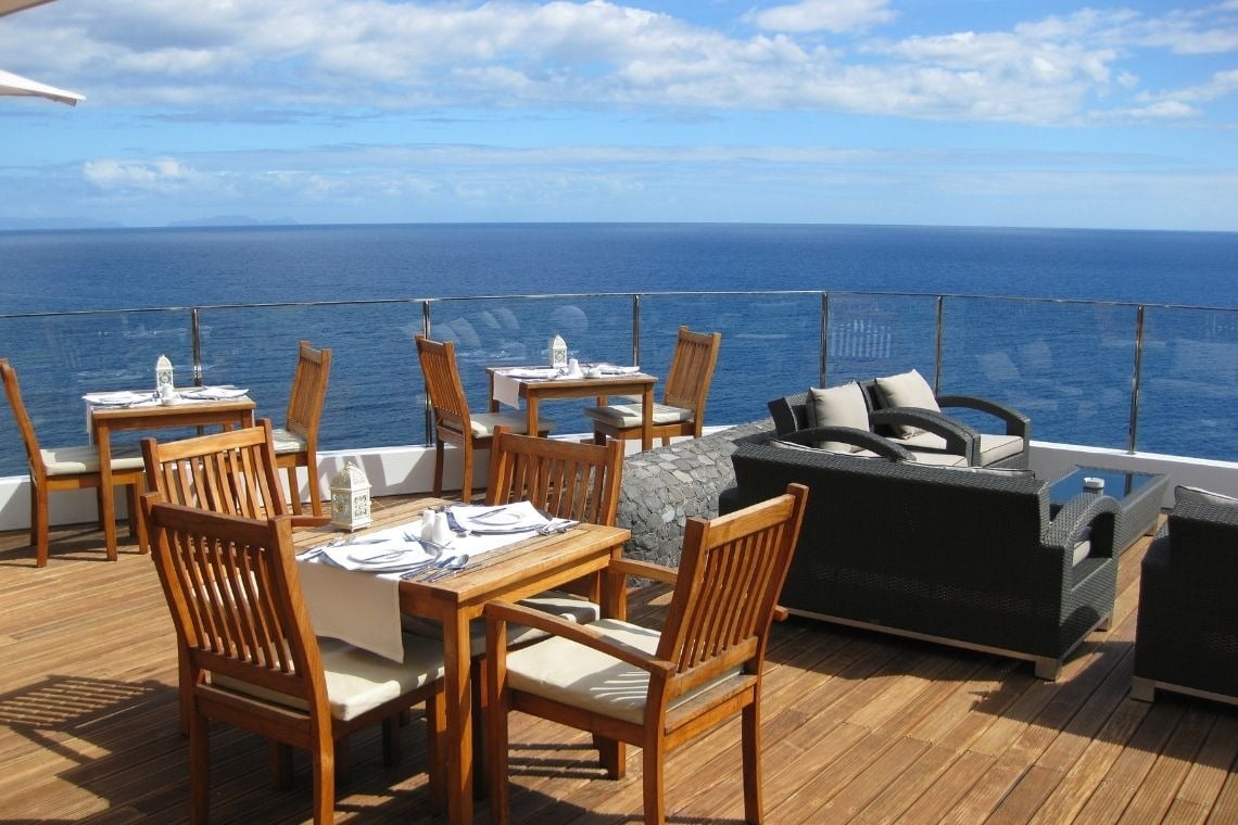mesas e cadeiras em um deck de madeira com vista para o oceano