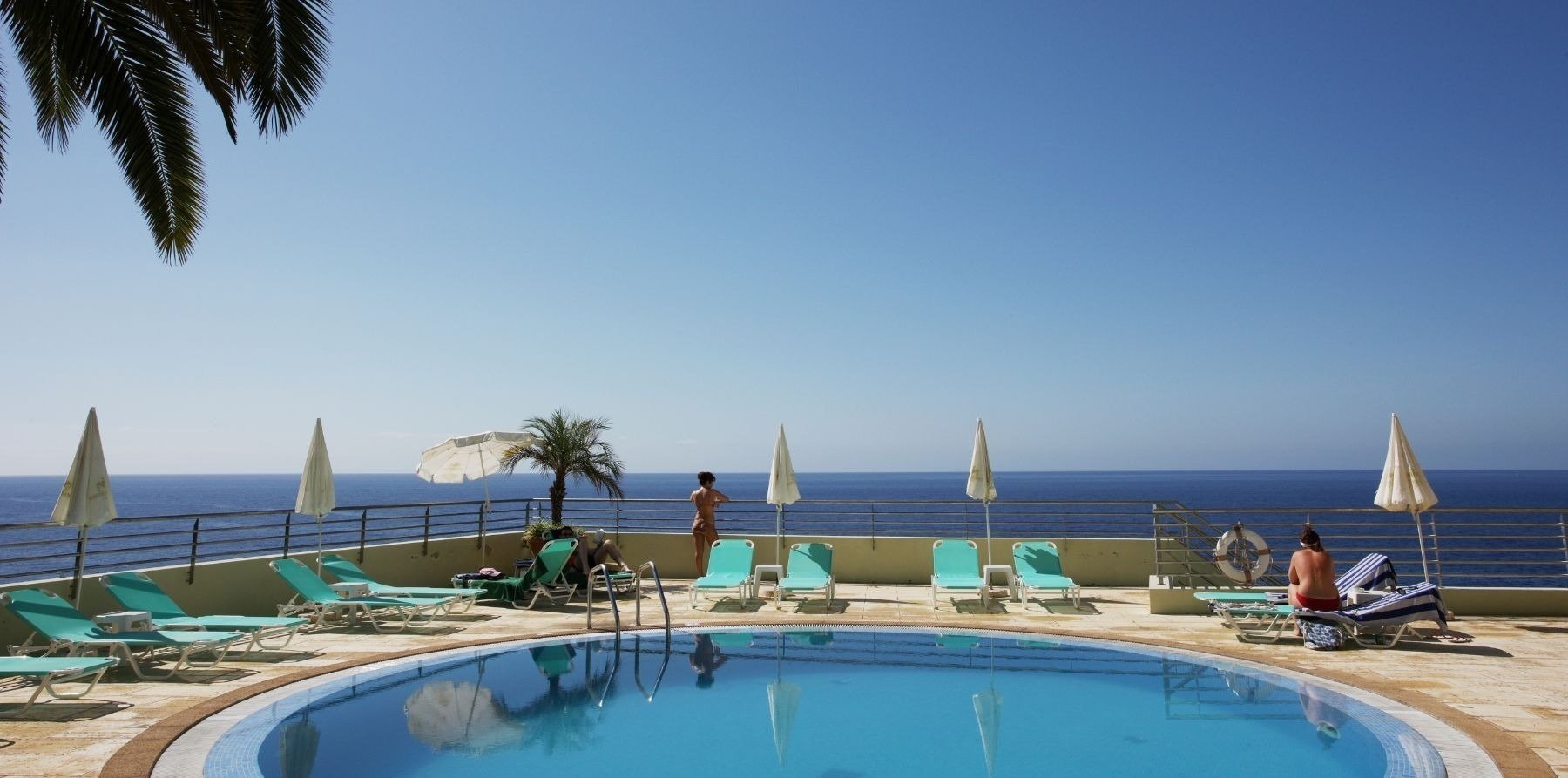 um grupo de pessoas ao redor de uma piscina com vista para o oceano