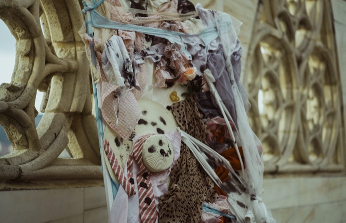 Textile art installation on a balcony with ornate stonework and a Gothic window. Maisonnave Hotel.